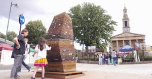 A family observing Plastic Mountain - a large tall pyramid made of rammed earth with little glints of plastic litter embeded in the layers.