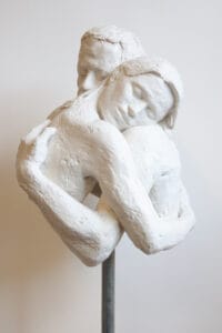 'Peaceful Embrace' a bonded marble sculpture, front view showing the interlocking arms of both figures. The two forms dissolve into one another at the chest.